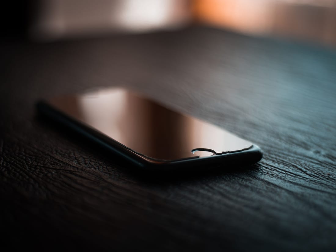 Un telefono appoggiato su un tavolo scuro, con lo schermo spento