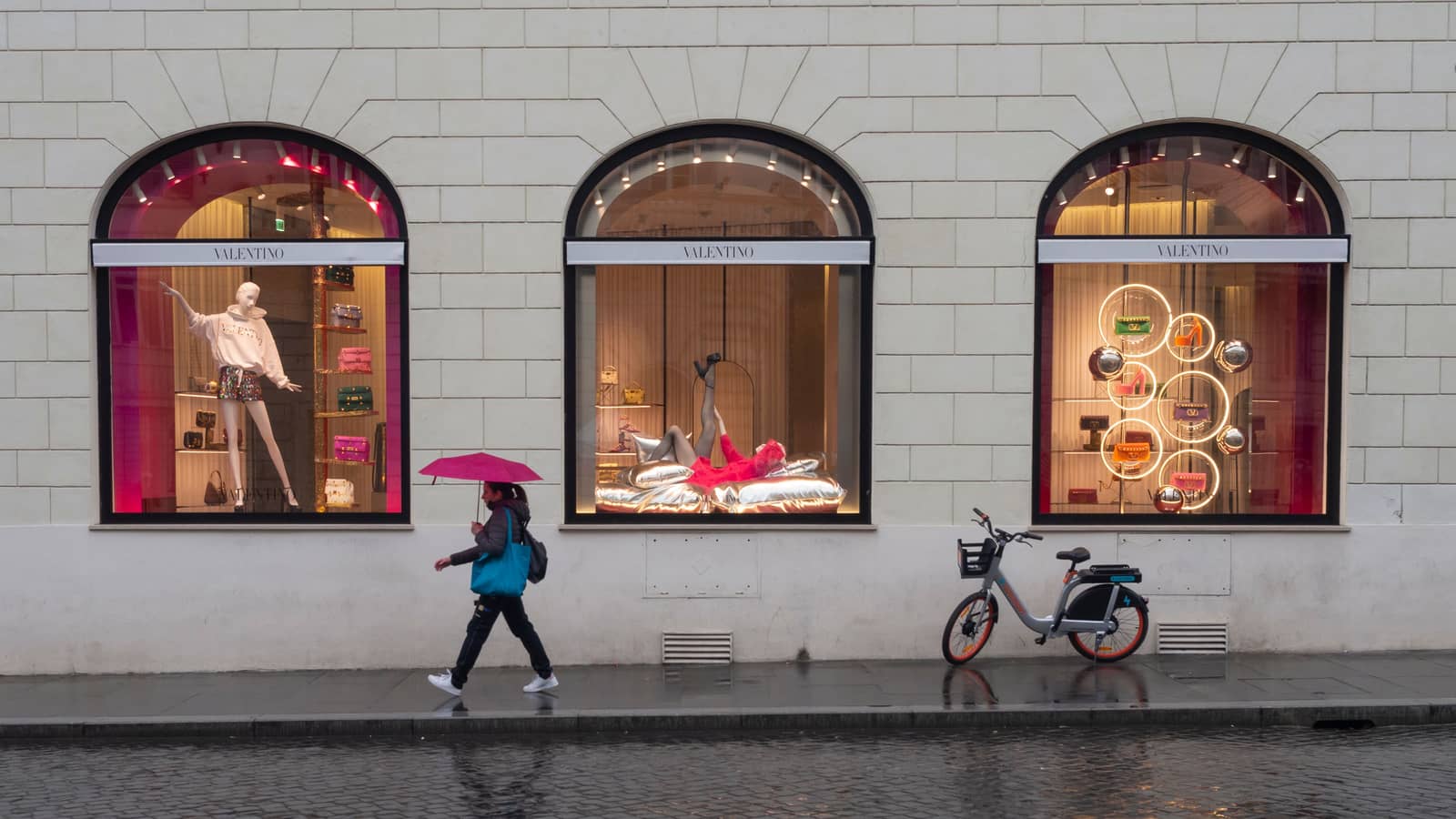 Tre vetrine illuminate in una via del centro di Roma, e una passante che tira dritto